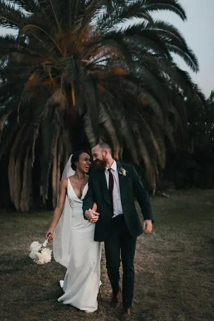 Mariage entre une femme à robe blanche et un homme en costume vert, sous les palmiers.