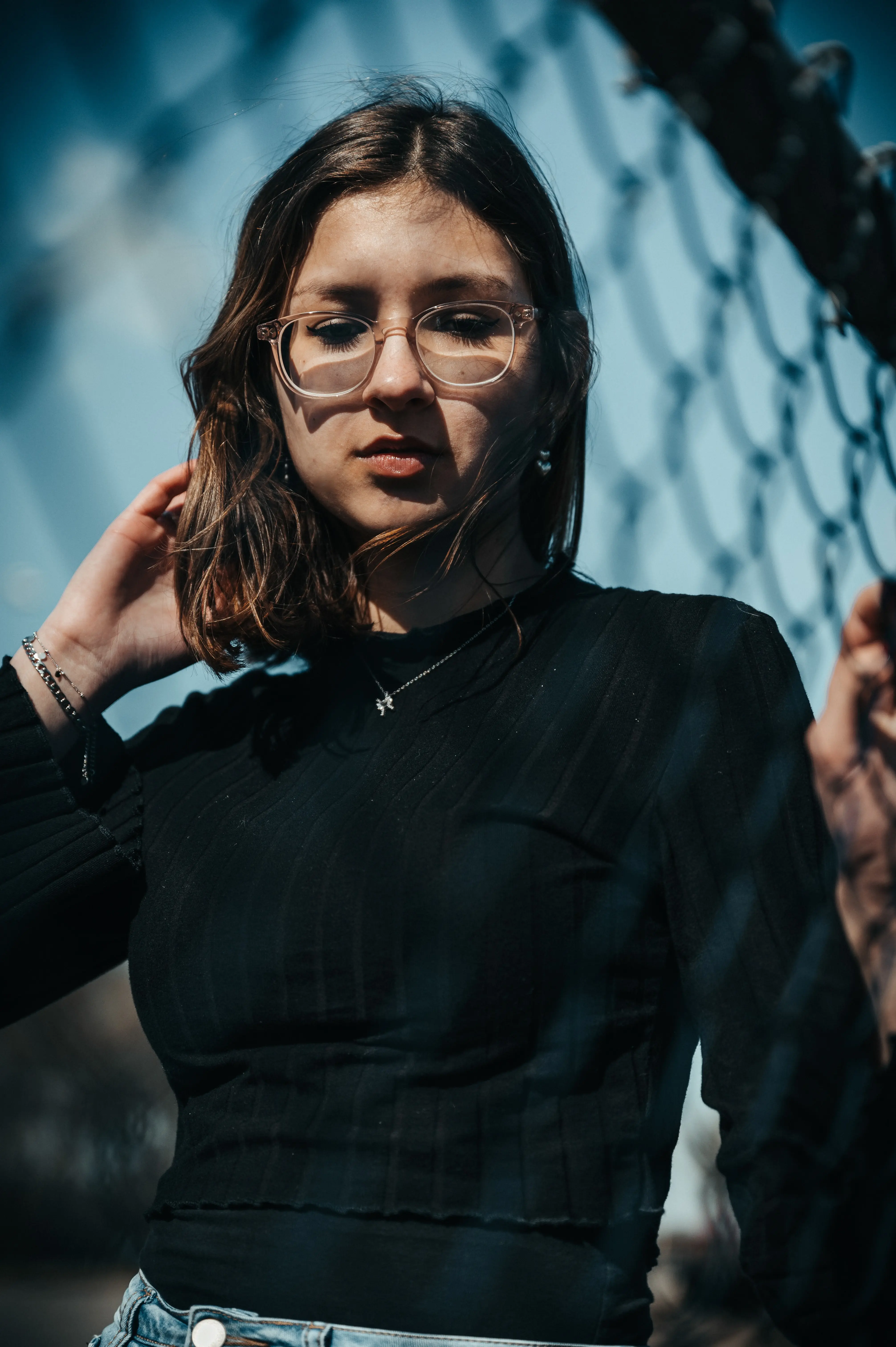 Portrait d'une jeune femme à lunette, t-shirt noir, en extérieur et beaucoup de bijoux.